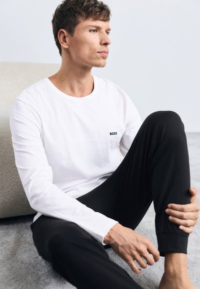 Chemise blanche à manches longues avec un col rond et un petit logo noir "BOSS" sur la poitrine, associée à un pantalon noir. Tissu doux, coupe décontractée.