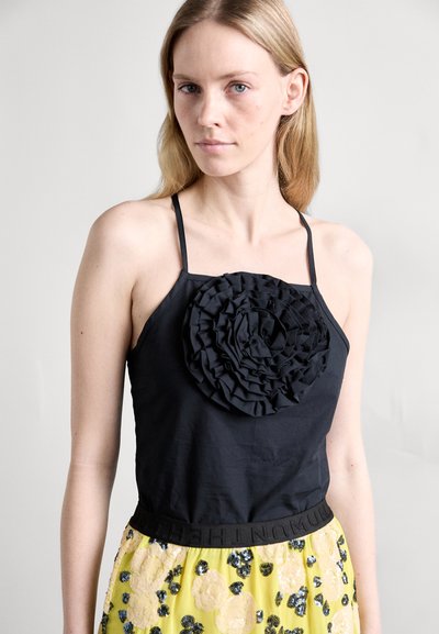 Black spaghetti strap top featuring a textured, ruffled flower detail at the center, paired with a yellow skirt adorned with floral and sequin patterns.