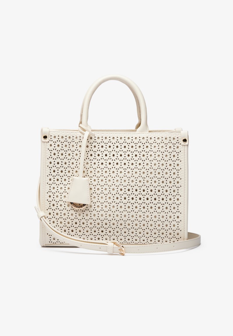 White handbag featuring a laser-cut pattern, structured shape, top handles, detachable shoulder strap, and a small, matching tag.