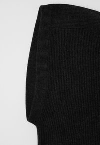 Dettaglio di un maglione nero a coste, che mette in evidenza una texture spessa, un design piegato e una finitura liscia. Il tessuto appare morbido e caldo.