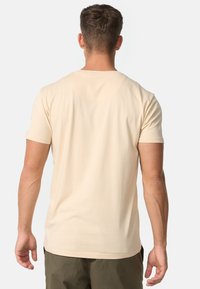 Rövid ujjú, kerek nyakú, világos bézs színű póló, puha pamutból készült, egyszerű mintával és minimális varrási részletekkel.