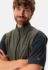 Weste mit hohem Kragen aus olivgrünem Stoff, Reißverschluss und dunklen kurzen Ärmeln mit strukturiertem Muster und Logo auf der Brust.