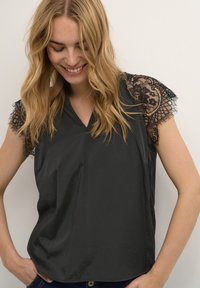 Top corto a maniche corte nero con scollo a V, caratterizzato da dettagli in pizzo testurizzato sulle spalle e una finitura liscia e lucida. Vestibilità casual e tessuto leggero.