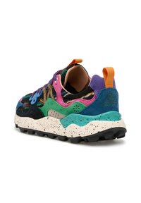 Sneaker coloré avec des panneaux verts, violets, roses, teal et noirs, semelle blanche avec des éclaboussures, étiquette orange, et semelle extérieure texturée noire vue de l'arrière.