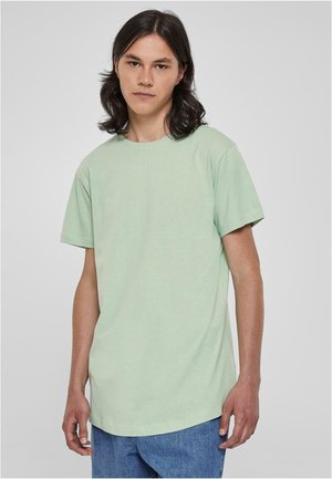 T-shirt en coton vert clair avec un col rond et des manches courtes, offrant une coupe décontractée et un ourlet légèrement allongé. Porté avec un jean bleu.