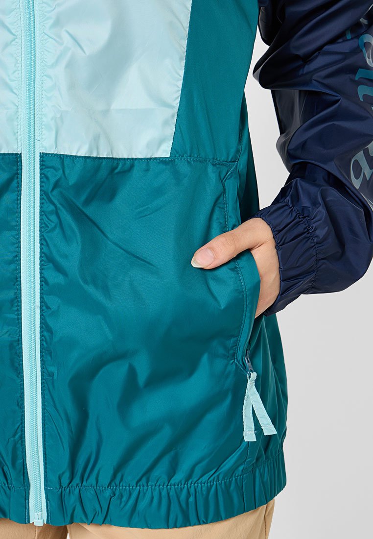 Teal und marineblau Windbreaker-Jacke mit einem Reißverschluss, elastischen Bündchen und einer Tasche mit einem hellblauen Reißverschluss, die eine glatte, glänzende Textur aufweist.