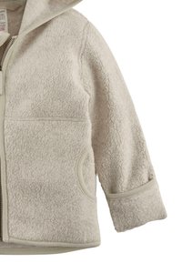 Fleecejacke mit einer strukturierten, cremfarbenen Außenseite, ausgestattet mit einem Reißverschluss, Kapuze und seitlichen Taschen. Abgesetzt mit kontrastierenden hellbeigen Akzenten.