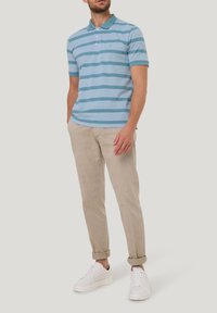 Korte mouw, lichtblauw gestreept polo t-shirt van katoen. Gecombineerd met beige opgerolde broek en witte sneakers. Eenvoudig ontwerp met knoopsluiting.