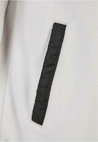 Gros plan d'un tissu blanc avec un patch rectangulaire noir vertical cousu dessus.
