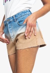 Pantalones cortos de mezclilla con un diseño ombré que transita de azul claro a marrón, con bordes deshilachados y un estilo clásico de cinco bolsillos.