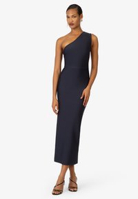 Robe ajustée bleu marine à une épaule, en tissu extensible, longueur au sol avec une silhouette épurée. Associée à des sandales noires à lanières.