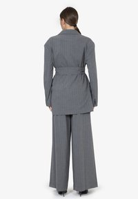 Completo grigio a righe sottili composto da un blazer lungo con cintura e pantaloni a gamba larga. Texture liscia e vestibilità sartoriale, mostrato di spalle.