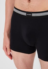 Svarta boxershorts tillverkade av ett mjukt tyg, med ett svart midjeband med grå ränder och en logotyp, tight passform och inga synliga mönster.