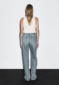 Jeans azzurro chiaro a vita alta con una vestibilità rilassata, dotati di due tasche posteriori e cuciture in vista, indossati con un top a canottiera bianco aderente.