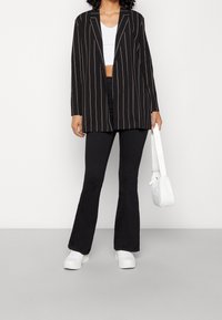 Svart- och vitrandig kavaj med lös passform och långa ärmar, matchad med svarta utsvängda byxor och vita sneakers. Vit handväska.