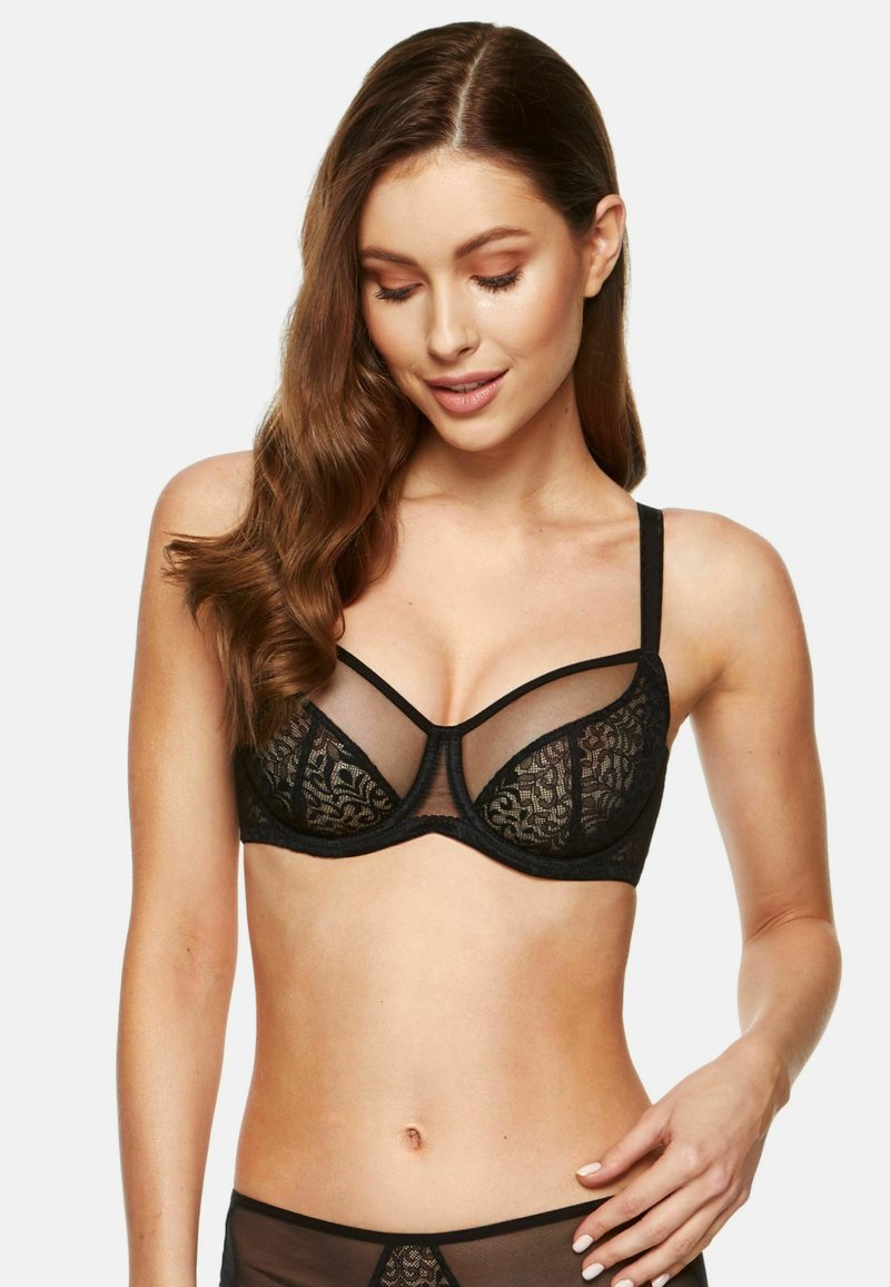 Czarny koronkowy biustonosz z przezroczystymi panelami siateczkowymi, wsparciem w postaci fiszbin, dekoracyjnym wykończeniem i regulowanymi ramiączkami, ozdobiony kwiatowym wzorem i gładką teksturą.