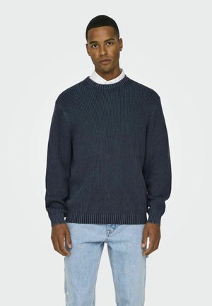 Donker marineblauwe geribbelde gebreide trui met een ronde hals, met lange mouwen en een textuurafwerking, gecombineerd met lichtblauwe spijkerbroeken.