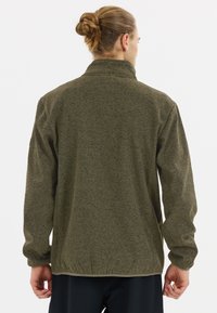 Fleecejacka i mörk olivgrön med texturerad yta, hög krage och elastisk nederkant. Har långa ärmar med diskreta sömdetaljer.