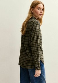 Camicia a quadri verde e nera con maniche lunghe, polsini abbottonati e colletto classico, abbinata a jeans blu a vita alta.