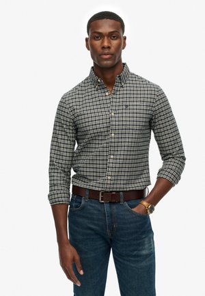 Camicia button-up con motivo a quadri in blu navy e bianco, maniche lunghe e colletto a punta, abbinata a jeans blu e una cintura marrone.
