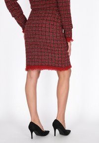 Piros és fekete tweed szoknya texturált mintázattal és rojtos szegéllyel, fekete velúr magassarkúval párosítva. A szoknya térd alá illeszkedő tervezésű.