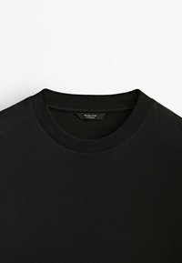 T-shirt noir à col rond en coton lisse, avec un col côtelé et sans graphismes ni motifs visibles.