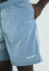 Fénykék színű, sima, könnyű anyagból készült rövidnadrág, oldalsó zsebekkel és fehér "carhartt" logóval az alján.