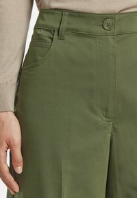 Gröna bomullsblandade byxor med en slät textur, med knappstängning, framfickor och sömdetaljer.