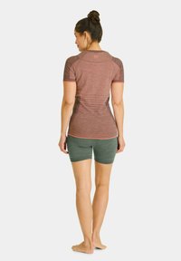 Short-sleeve, fitted top in reddish-brown, with light accent stitching, paired with dark green shorts. Soft, stretchy fabric, athletic design.