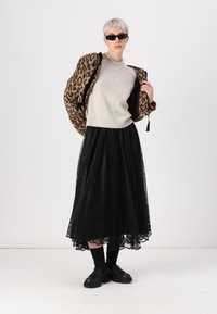 Leopardo rašto striukė, pilka megztinis su perlų akcentais, juoda nėrinių maksi sijonas, juodos kojinės ir masyvūs batai. Minimalistiniai saulės akiniai ir auskarai-žiedai.