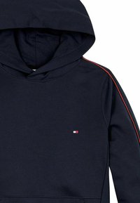Felpa navy con cappuccio regolabile, strisce rosse accenti sulle maniche e un piccolo logo sul petto. Tessuto morbido.