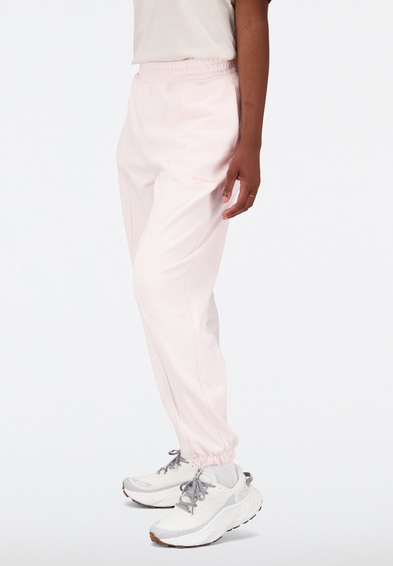 Pantalon de sport rose clair avec une coupe ajustée et une taille élastique ; il présente des poches latérales et un logo de marque subtil sur la jambe.