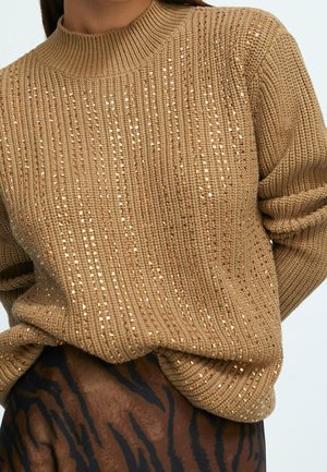 Beżowy sweter z dzianiny z małymi złotymi cekinami, noszony wpuszczony w brązową i czarną spódnicę w zwierzęcy wzór.