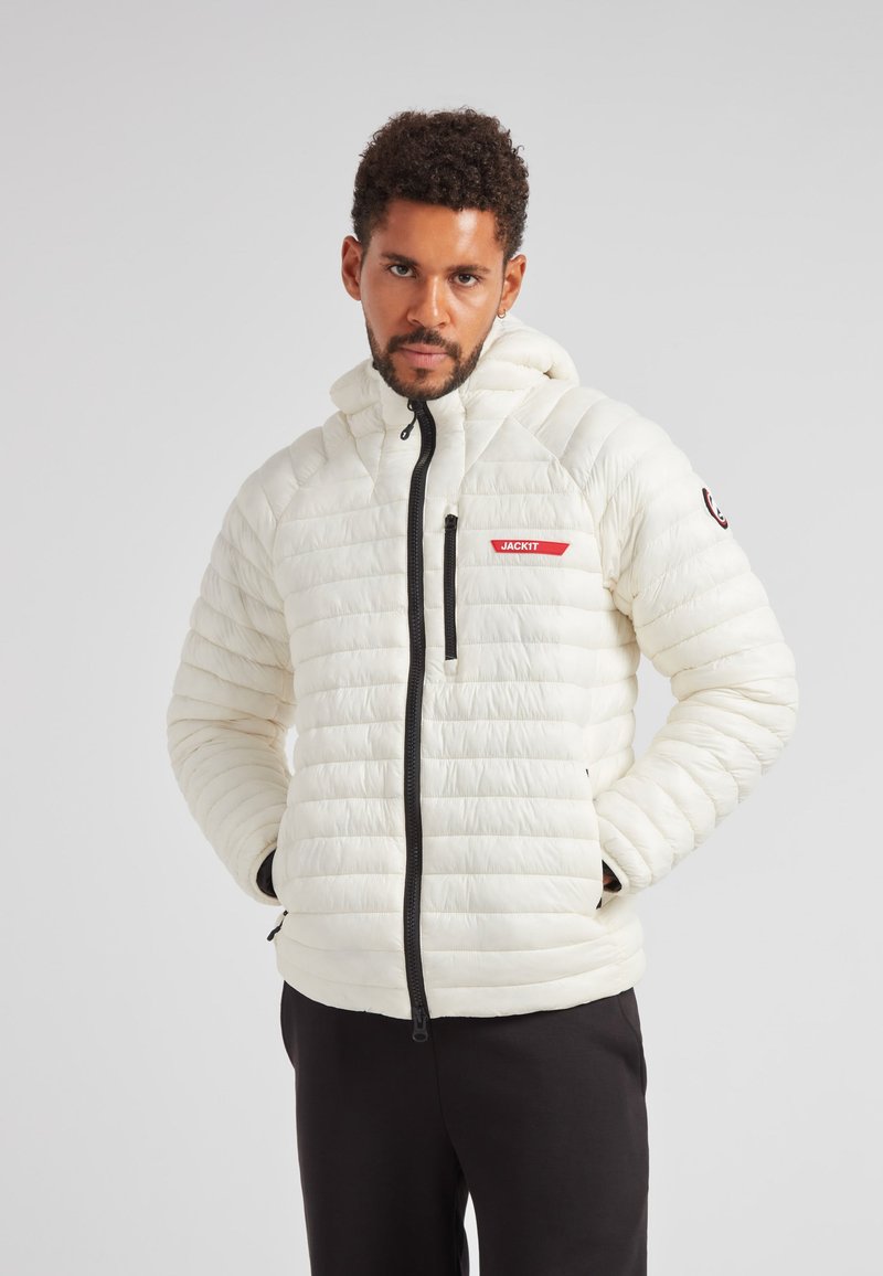 Giacca a vento bianca con motivo trapuntato orizzontale, chiusura con zip e cappuccio regolabile. Presenta un marchio rosso e cerniere nere.