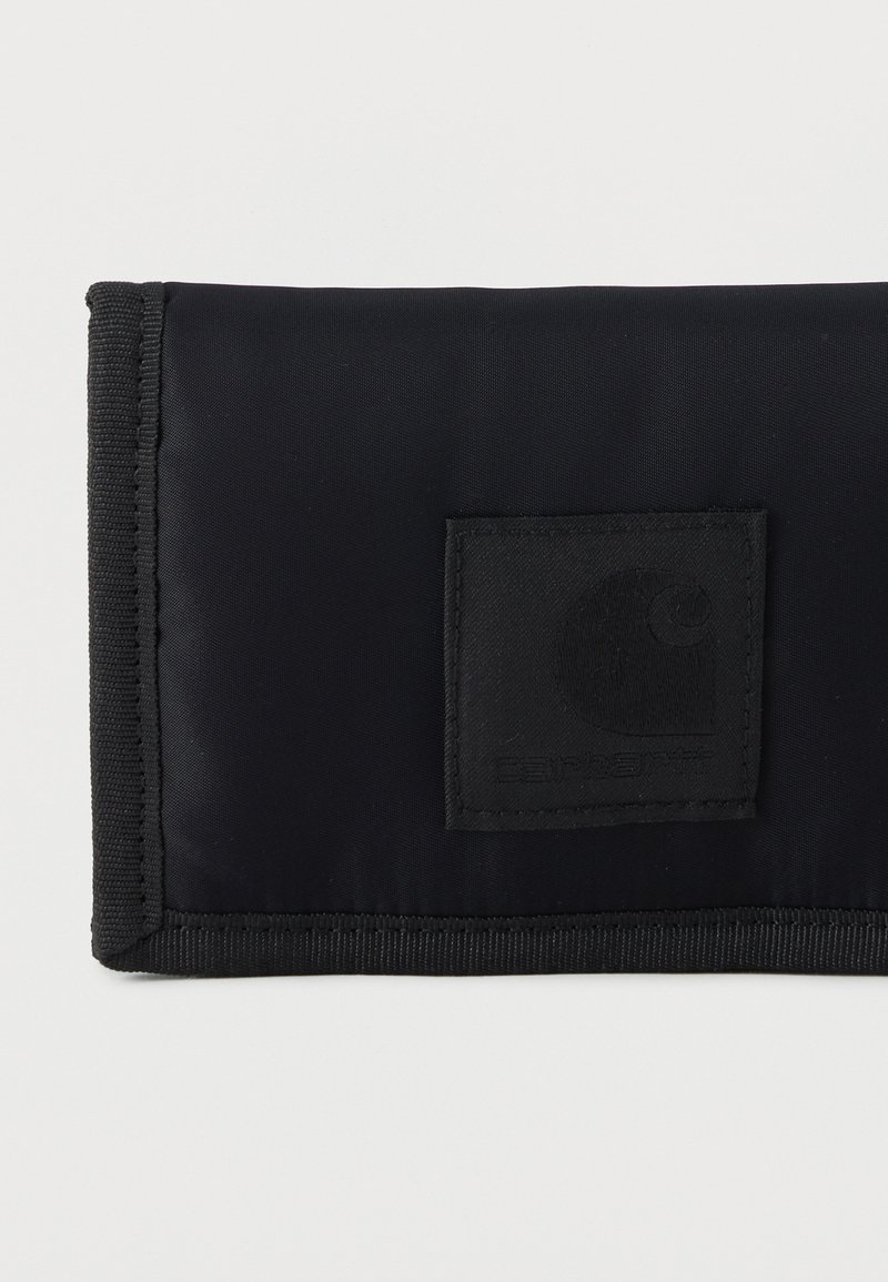 Cartera de tela negra con bordes reforzados y un parche cuadrado cosido con un logo sutil en relieve sobre un fondo liso.