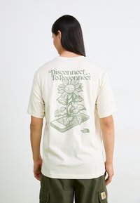 Cream-colored t-shirt with a graphic of a sunflower and text “Disconnect To Reconnect” in green, featuring a relaxed fit and short sleeves.