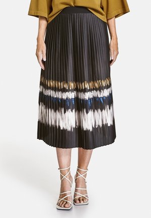 Mujer llevando una falda midi negra plisada con rayas horizontales multicolor efecto tie-dye, top color camello y sandalias blancas de cordones.