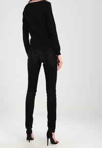 Maglione nero con scollo rotondo, maniche lunghe e rifinitura texturizzata. Indossato con jeans skinny neri e scarpe con tacco.