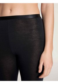 Leggings neri con una cintura liscia ed elastica, realizzati in un tessuto morbido e leggermente trasparente. Presentano un design aderente.