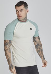 Short-sleeve baseball t-shirt, cream body with teal sleeves, featuring a small black logo on the chest. Smooth fabric, fitted cut.