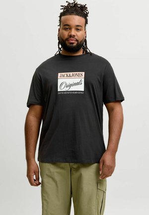 Mand med dreadlocks iført en sort "Jack & Jones Originals" t-shirt og kaki cargobukser, stående mod en ensartet lys baggrund.