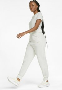 Completo activewear grigio chiaro composto da una maglietta a maniche corte e pantaloni jogger con vita elastica, abbinato a sneakers bianche e un marchio discreto.