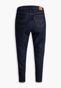 Jeans de denim azul oscuro con un ajuste slim, cuentan con bolsillos traseros, costuras doradas y un parche de cuero en la cintura.