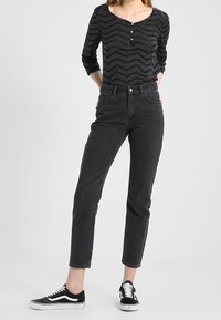 Svart långärmad topp med zigzag-mönster, hög midja svarta jeans och svarta kanvas sneakers med vita sulor.