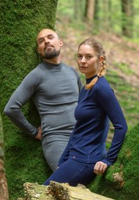 Magliette a manica lunga attive in grigio e blu navy indossate da due modelli, appoggiati a degli alberi coperti di muschio in un ambiente boschivo.