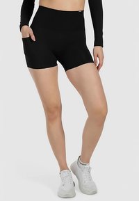 Zwarte shorts met hoge taille en een gladde textuur, voorzien van zijzakken en een getailleerd ontwerp, gecombineerd met witte sportschoenen.