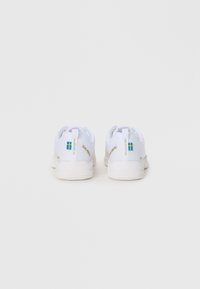 Chaussures de sport blanches avec un tissu texturé, des semelles rembourrées et des accents de marque bleu et or sur le talon.