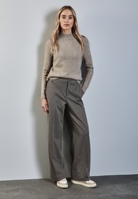 Beige trui met een hoge geribbelde kraag, grijs gestreepte wijde broek en lichtgekleurde sneakers met gelaagde ontwerpen.