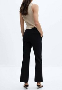 Beżowy prążkowany top bez rękawów połączony z czarnymi spodniami dzwonami, które mają boczne kieszenie i gładkie wykończenie materiału. Czarne szpilki dopełniają całość.