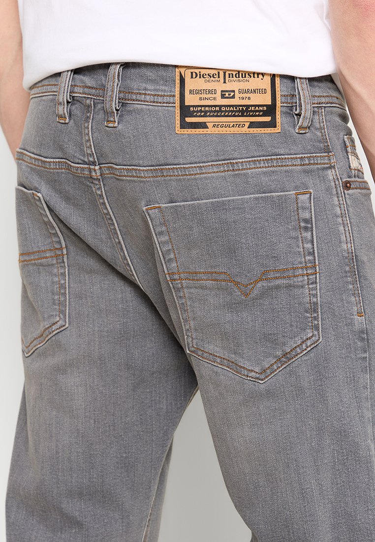 Grijze denim jeans met een tan leren achterkant label. Beschikt over dubbele achterzakken met een decoratief stikselpatroon en oranje accenten.